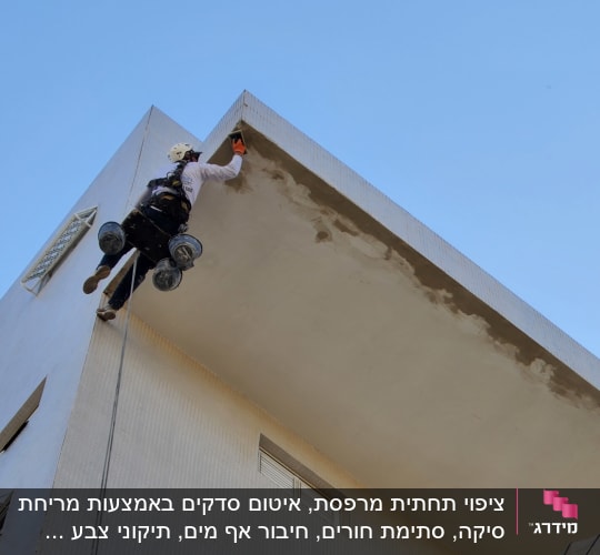 עובד בגובה על חבל צובע קיר חיצוני